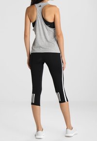 Top senza maniche grigio con apertura sulla schiena, abbinato a leggings neri a tre quarti con tre strisce bianche su ciascun lato. Scarpe sportive bianche.