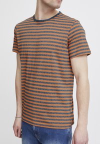 Orange and navy blue striped t-shirt made of soft fabric with a round neck and short sleeves, featuring side slits for ease of movement.