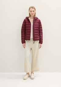 Bordeaux pufferjack met horizontale stiksels en capuchon, gecombineerd met lichtbeige wijde broek en platform loafers.