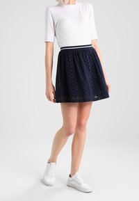 Námořnická modrá sukně s texturou a designem s očky, stažený pas a odpovídající elastický pas, spárována s bílým tričkem s krátkým rukávem a bílými teniskami.