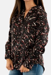 Camisa negra de botones de manga larga con un patrón abstracto en rojo y crema, que cuenta con un cuello, mangas con puños y un dobladillo ligeramente curvado.