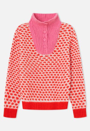 Pleteni pulover z vzorcem rdečih in belih zvezd ter roza rebrastim ovratnikom in tremi roza gumbi ob izrezu.