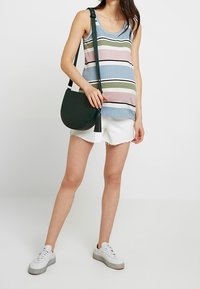 Randig linne i blått, rosa och grönt, parat med vita shorts. Accessoriserad med en rund mörkgrön axelremsväska och vita sneakers.