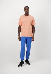 Men's outfit featuring a light pink cotton t-shirt and blue elastic cuff joggers, paired with black athletic shoes.