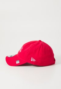 Cappello rosso in cotone con visiera curva, dotato di dettagli ricamati e fori di ventilazione. Il logo è stampato sul fronte e sul lato.