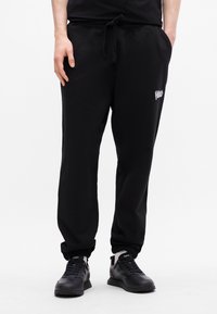 Schwarze Jogginghosen mit elastischem Bund und verstellbarem Kordelzug, mit Seitentaschen und gerippten Bündchen. Dezentes Logo an der Hüfte.