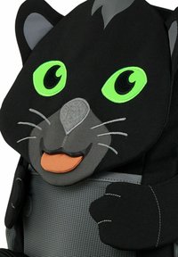 Schwarzer Stoff-Rucksack mit einem Katzenkopfdesign, großen grünen Augen, grauen Akzenten und einem orangefarbenen Zungendetail. Netzfach auf der Vorderseite.