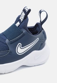 Námornícky modrá športová obuv s elastickým popruhom, sieťovanými detailmi a bielou gumovou podrážkou. Obsahuje výrazné biele logo Nike swoosh a zadný úchyt.