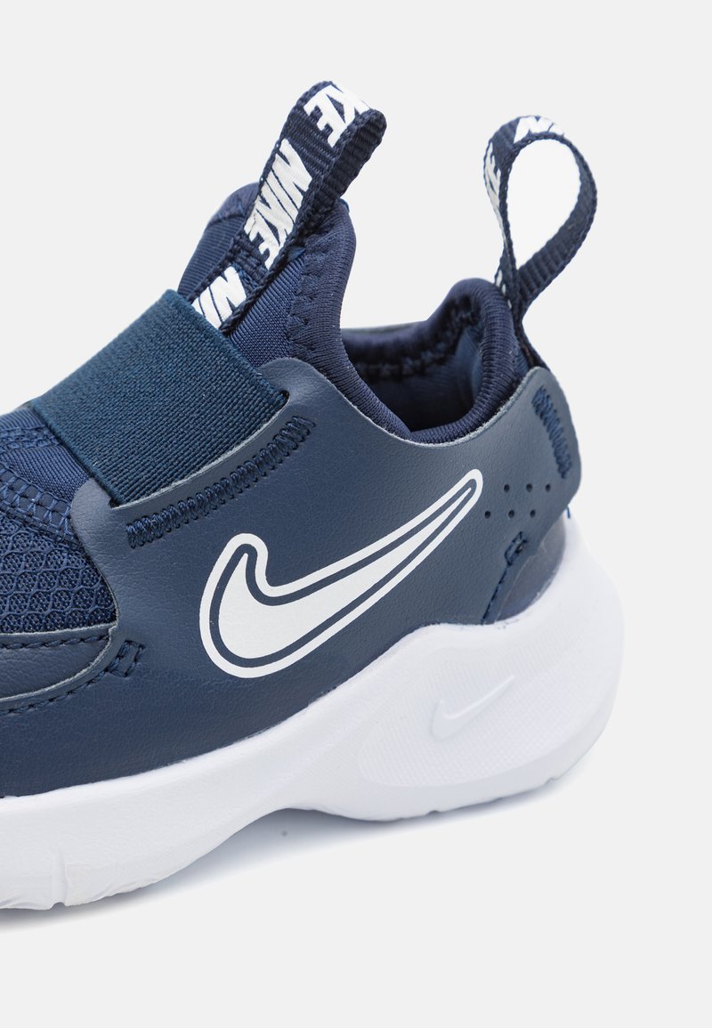 Scarpa sportiva blu navy con fascia elastica, dettagli in rete e suola in gomma bianca. Presenta un grande logo Nike bianco e una linguetta sul retro.
