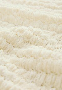 Gestructureerde crème stof met een golvend patroon, met zachte, verhoogde strepen die diepte en visuele interesse creëren. Lichtgewicht en luchtige uitstraling.