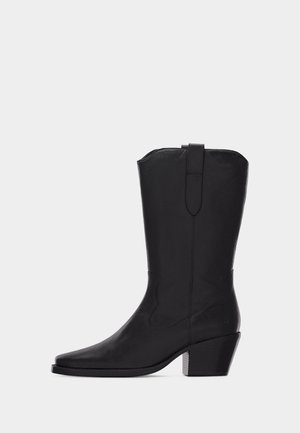 Stivale western nero in pelle fino al polpaccio con punta appuntita, tacco a blocco e dettagli cuciti su sfondo semplice.