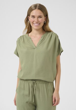 Haut vert olive à manches courtes avec un col en V, texture douce et détails froncés aux épaules, associé à un pantalon à cordon de serrage assorti.