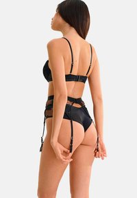 Ensemble de lingerie noire comprenant un bralette en dentelle avec des bretelles réglables, des détails transparents, et une ceinture porte-jarretelles avec des clips et des accents en découpe.