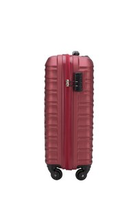 Valise rigide de couleur rouge profond avec une surface texturée, des rainures verticales et une fermeture éclair rouge contrastante. Équipée de quatre roues noires et d'un verrou.