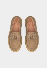 Ζευγάρι μπεζ σουέτ μοκασίνια με λαστιχένιες σόλες και κορδόνια, με ετικέτα "AGL" στο εσωτερικό, σε λευκό φόντο, φωτογραφημένα από πάνω.