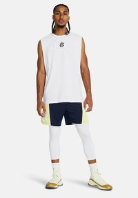 Weißes ärmelloses Top, marineblaue und gelbe Shorts, weiße Kompressionsleggings und Sneakers mit goldenen Akzenten. Auffälliges Logo auf der Brust.