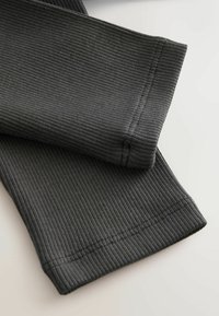 Čierne rebrované legíny s priliehavým strihom, hladkým povrchom, kontrastným prešívaním a stredne vysokým pásom.