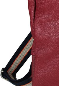 Close-up van een rode, gestructureerde leren tas met een verstelbare band in zwart, beige en oranje met strepen en zilverkleurige metalen hardware.