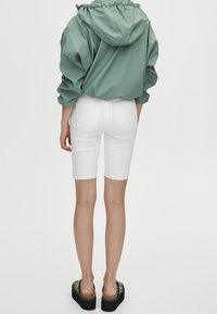Chaqueta verde con capucha, pantalones cortos de mezclilla blancos y sandalias de plataforma con un diseño de cebra. La chaqueta tiene una capucha fruncida y un corte relajado.