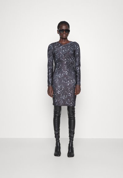 Dlhé šaty z tmavého materiálu s abstraktnými bielymi vzormi. Priliehavý strih, okrúhly výstrih, doplnené lesklými čiernymi čižmami nad kolená.