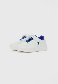 Baskets Champion blanches avec des lacets bleus, une doublure intérieure bleue et une sangle Velcro sur fond blanc.