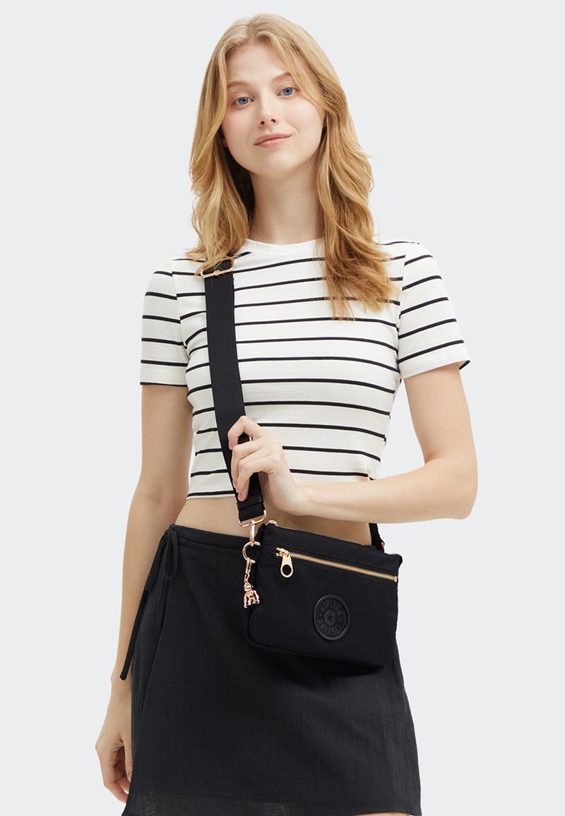 Borsa a tracolla in tessuto nero con hardware dorato, tasca con zip e logo impresso. Caratterizzata da una tracolla regolabile e da una forma rettangolare.