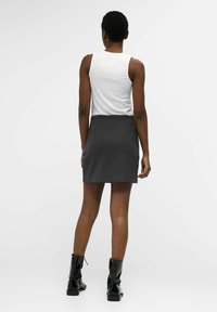 Un haut sans manches blanc associé à une jupe noire ajustée, longueur genou, présentant une texture lisse et des poches latérales. Des bottines noires à la cheville sont portées.
