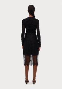 Black long-sleeve top with ruched texture, paired with a black lace skirt featuring a sheer hem and intricate floral patterns.
