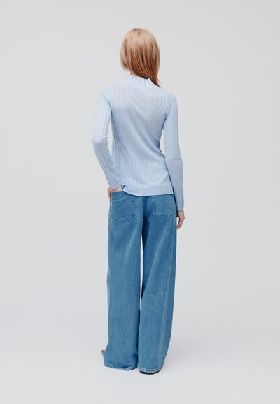 Top azzurro chiaro a maniche lunghe con righe a coste abbinato a jeans blu a gamba larga e morbida; texture morbida, sottili righe verticali e tasche a toppa.