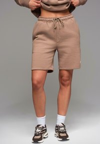 Beige šortky z bavlněné směsi s elastickým pasem a šňůrkou, s bočními kapsami a malou nášivkou s logem. Nosené se sportovními teniskami.