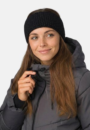 Young woman adjusting the zipper on a gray winter jacket, wearing a black knitted headband, with long brown hair and a slight smile.