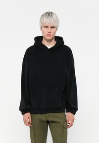 Zwarte fleece hoodie met een voorzak en lange mouwen. Voorzien van een trekkoordcapuchon en een ontspannen pasvorm. Gemaakt in combinatie met olijfgroene cargobroek.