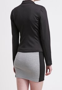 Černý přiléhavý blazer s hladkým povrchem, doplněný o vzorovanou mini sukni s geometrickým designem v černé a bílé barvě.