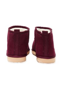 Burgundowe zamszowe botki za kostkę z miękkim białym wykończeniem, posiadające płaską, tanową gumową podeszwę i dwa materiałowe uchwyty ułatwiające zakładanie.