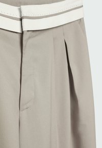 Pantalon beige clair à taille haute avec un pli et une ceinture blanche contrastante avec de petites perforations.