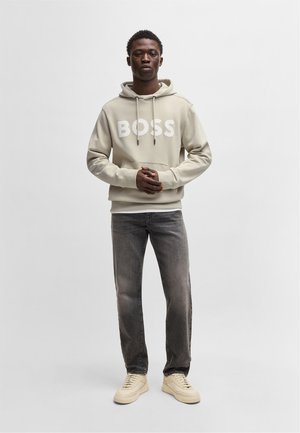 Felpa grigia chiara con grande logo bianco "BOSS", abbinata a jeans grigi scuri e sneakers beige. Texture liscia, vestibilità casual.