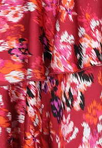 Röd tygmönster med stora, abstrakta blommönster i rosa, orange, vitt och svart. Mjuk textur med lager av volangdetaljer.
