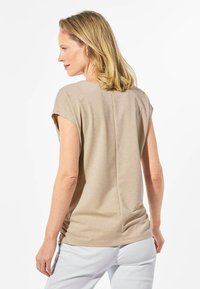 Beige Hemd mit kurzen Ärmeln, weichem Textil und leichtem Schimmer. Verfügt über eine lockere Passform und eine vertikale Naht auf der Mitte des Rückens.