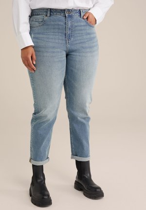 Helle blaue Jeans mit geradem Schnitt, hoher Taille, aufgerolltem Saum und vorderen Taschen, kombiniert mit schwarzen klobigen Stiefeln.