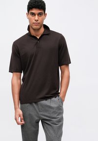 Kortermet, mørkebrun polo-skjorte med en myk tekstur, med knapper i kragen, kombinert med lysegrå, skreddersydde bukser.