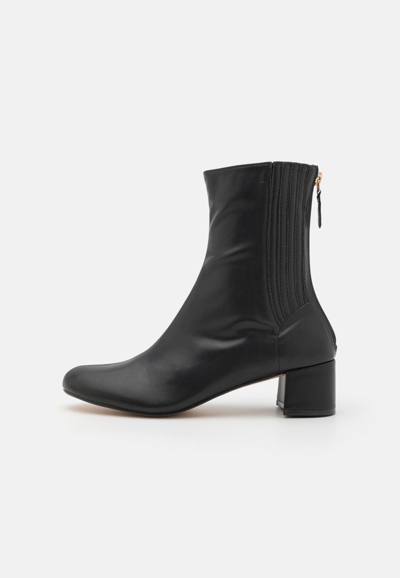 Botte en cuir noire mi-mollet avec talon bloc bas, panneaux élastiques latéraux et fermeture éclair arrière avec tirette sur fond blanc.