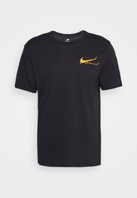 Svart bomullströja med en gul Nike-logotyp och text på framsidan. Korta ärmar, rundad halsringning och avslappnad passform. Slät textur.