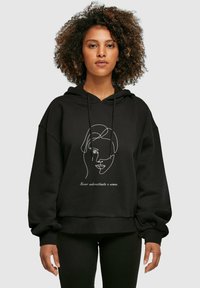 Svart oversized hoodie med en framgångsdesign av en kvinnas ansikte och text. Tillverkad av ett mjukt material med en mysig, texturerad yta.