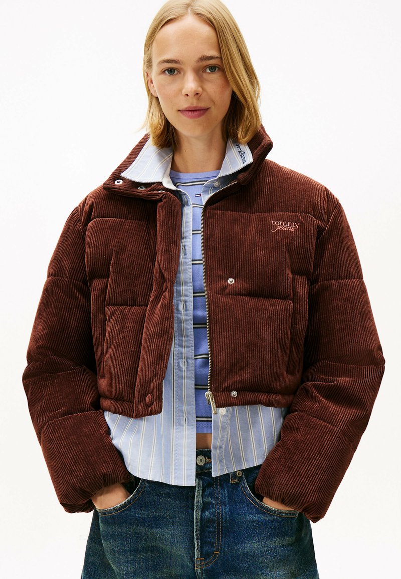 Brun corduroy pufferjakke med et cropped design, der har en høj krave, flere polstringssektioner og metaltrykknapper.