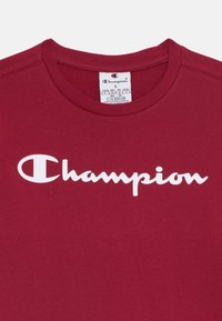 Bordeaux bomull t-skjorte med hvit "Champion" logo over brystet. Klassisk rund hals design med synlig stellabeltegn på halsen.