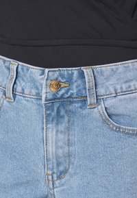 Ljusblå denimjeans med dragkedja, guldknappsstängning och orange sytråd. Har framfickor och en slät yta.