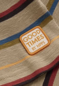 Beige Stoff mit mehrfarbigen Streifen in Rot, Blau, Gelb und Grün. Besitzt ein quadratisches oranges Patch mit der Aufschrift "GUTE ZEITEN BY NPPS."