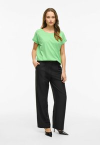 Grön kortärmad skjorta i mjukt tyg, matchad med höga svarta vida byxor. Svarta lackklackar fulländar outfiten.