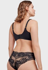 Soutien-gorge noir avec bretelles réglables et fermeture à crochets, en tissu lisse. Associé à un string noir en dentelle transparente avec des motifs floraux.