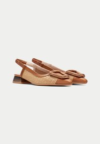 Zapatos slingback color marrón claro con textura trenzada, punta redonda y un adorno decorativo de nudo. Tacón bajo y angulado, y correa elástica para un ajuste perfecto.